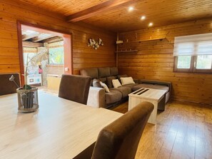 Ein gemütliches Blockhaus-Interieur mit Holzvertäfelung, einer Couch, einem Esstisch und einem Fenster.