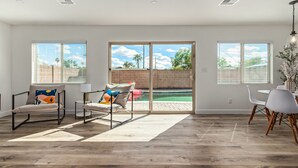 Ein geräumiges Zimmer mit einer großen Glasschiebetür, die zu einem Pool führt, einem Essbereich mit weißen Stühlen und einer Sitzecke mit zwei Stühlen und einem Tisch.