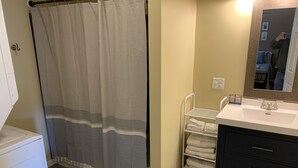 Un baño con cortina de ducha, un lavabo blanco, un espejo y un perchero para toallas.