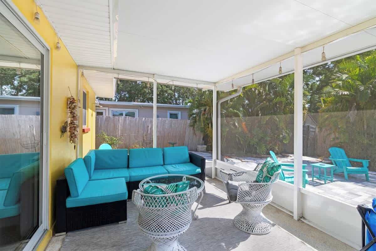 A covered patio area with a turquoise sofa, wicker chairs, and a pool.