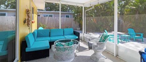 A covered patio area with a turquoise sofa, wicker chairs, and a pool.