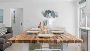 A modern dining area with a wooden table set for six, white walls, and a decorative wall art piece.