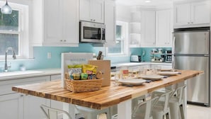 A modern kitchen with white cabinets, a wooden countertop, stainless steel appliances, and a welcome sign.