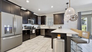 A modern kitchen with dark cabinets, stainless steel appliances, and a central island with seating. - Disney-Themed Family Retreat: Private Arcade & Pool w/Free Waterpark & Clubhouse (Four Corners)