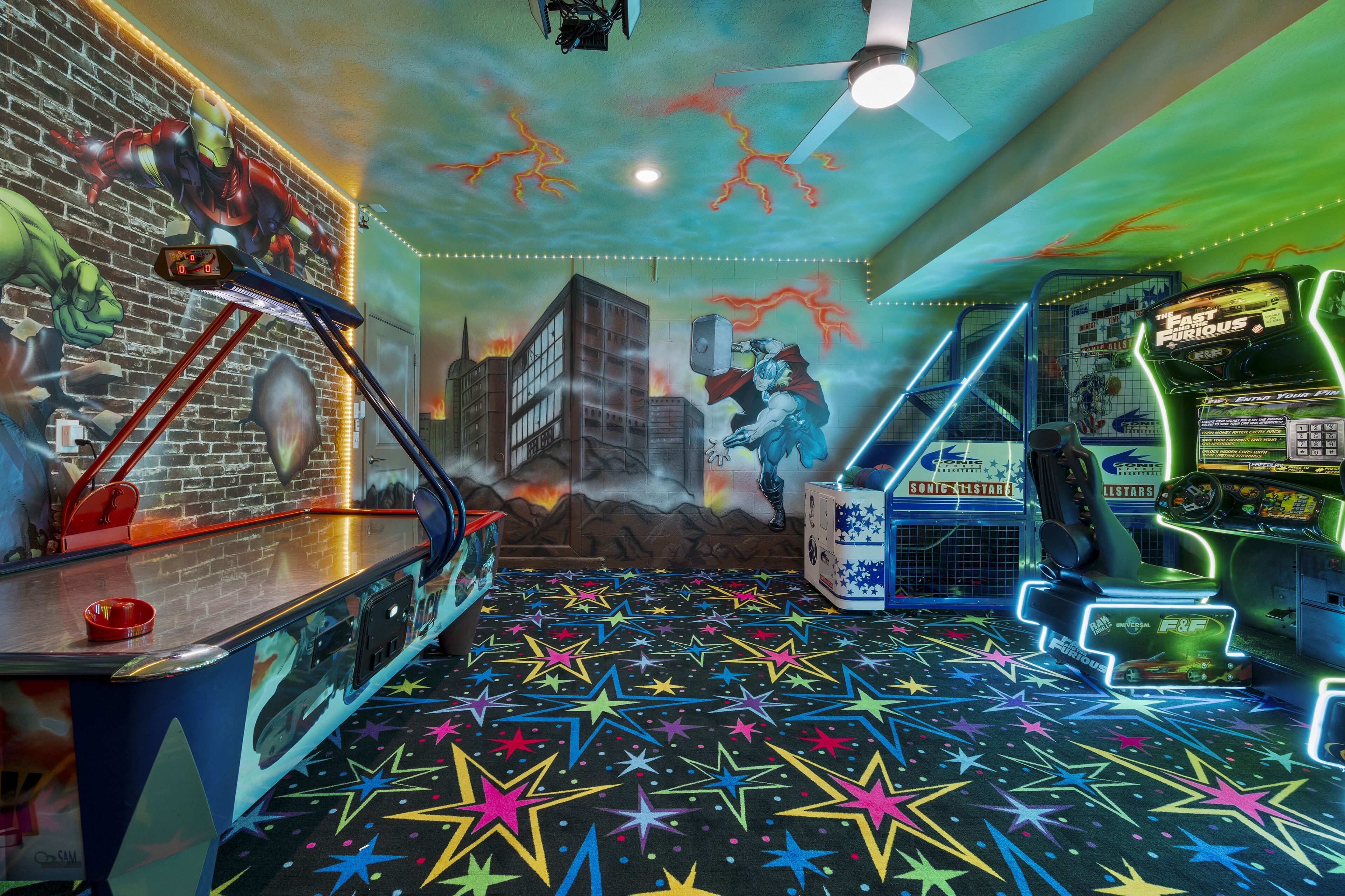 A vibrant arcade room with neon lights, a mural of superheroes, and a star-patterned floor.