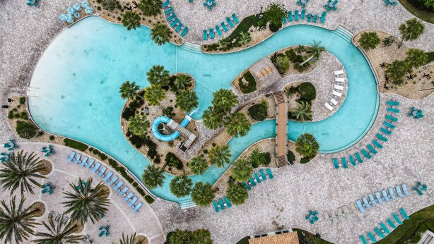 An aerial view of a resort with a large central pool, multiple lounge areas, and surrounding greenery. - Disney-Themed Family Retreat: Private Arcade & Pool w/Free Waterpark & Clubhouse (Four Corners)