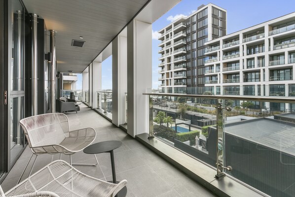 A modern balcony with white wicker chairs and a small table, overlooking a high-rise building and a pool area. - Elegant retreat in Wynyard Quarter (Auckland)