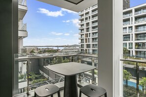 A balcony with a table and two chairs, overlooking a cityscape with modern buildings and a clear sky. - Elegant retreat in Wynyard Quarter (Auckland)