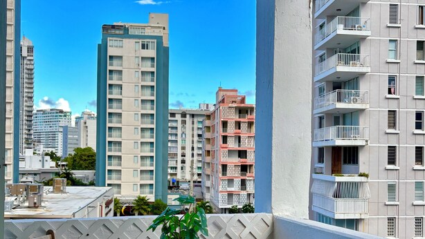 A balcony with a wooden table and chairs, a potted plant, and a view of surrounding buildings.