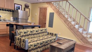 A cozy living room with a sofa, a coffee table, and a wooden staircase. - Wapiti Cabin - a Wolf Crossing Cabin next to Yellowstone (Silver Gate)