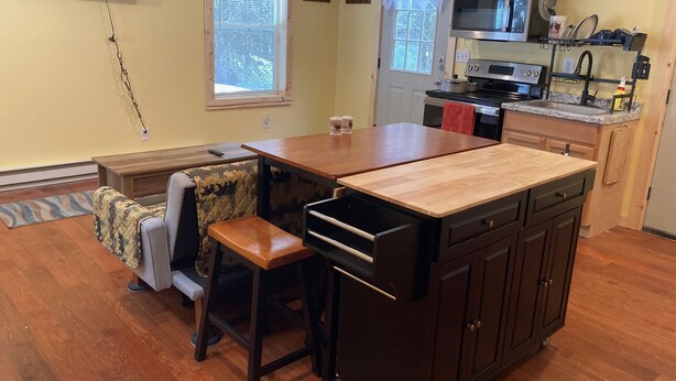 A compact kitchen with a wooden island, a dining table, and a sofa. - Wapiti Cabin - a Wolf Crossing Cabin next to Yellowstone (Silver Gate)