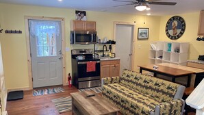 A compact living space with a kitchenette, a sofa, a dining table, and a ceiling fan. - Wapiti Cabin - a Wolf Crossing Cabin next to Yellowstone (Silver Gate)