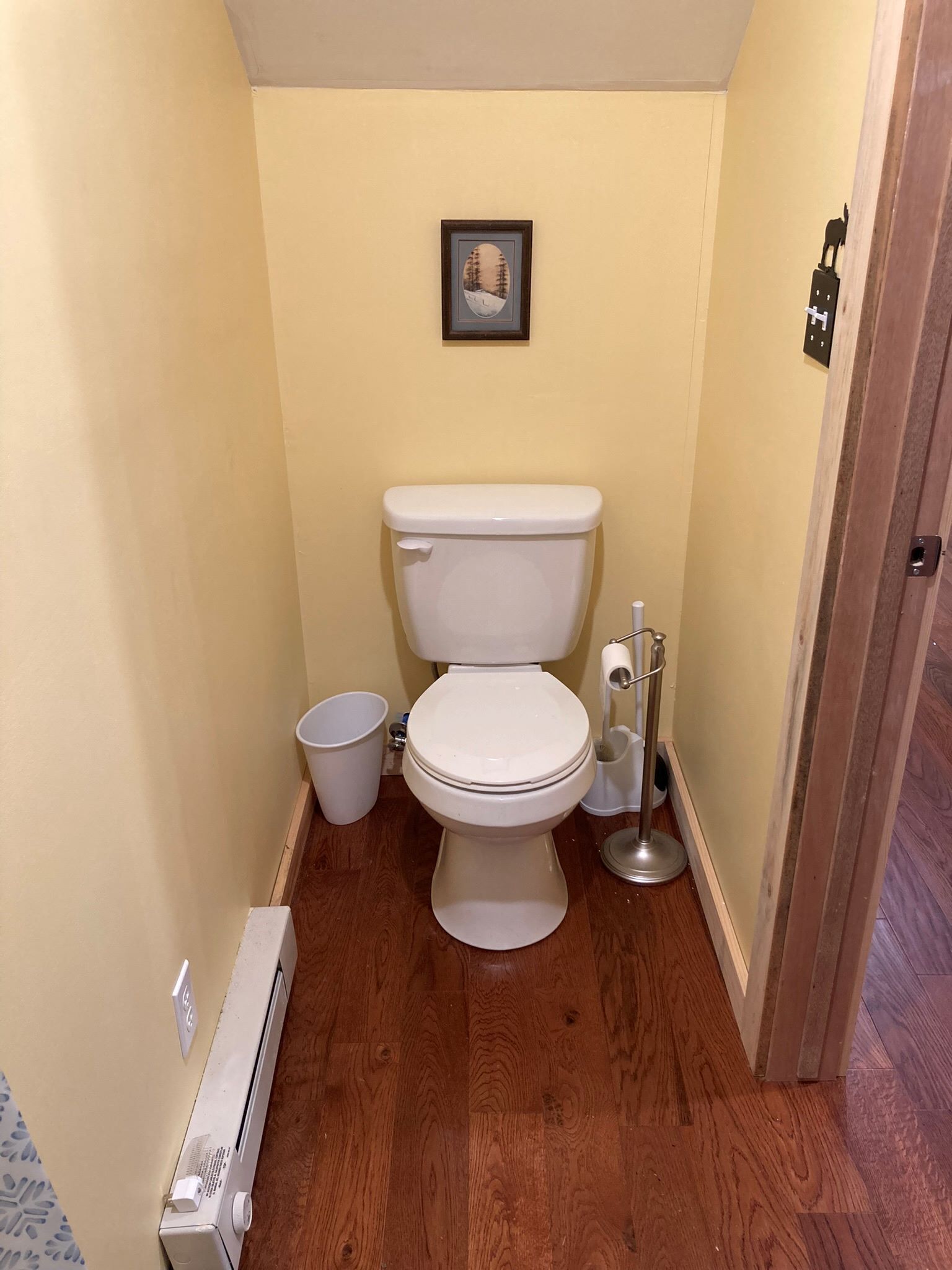Une petite salle de bain étroite, équipée de toilettes, d’une poubelle et d’un sèche-mains.