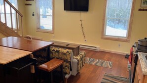 A cozy kitchen with wooden flooring, a dining table, a couch, and a TV mounted on the wall. - Wapiti Cabin - a Wolf Crossing Cabin next to Yellowstone (Silver Gate)