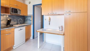 Une cuisine compacte avec des meubles en bois, un four à micro-ondes, une machine à café et une petite table.