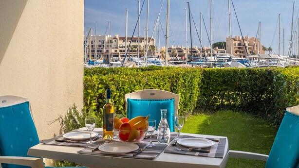 Un espace de restauration en plein air avec une table dressée pour deux personnes, donnant sur une marina où sont amarrés de nombreux bateaux.