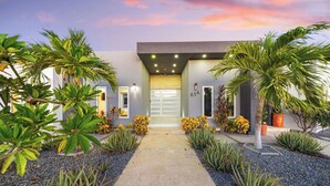A modern house with a central entrance, surrounded by tropical plants and a gravel pathway. - Modern & Spacious 4BR3BA w/ Pool & Close to Beach! (Noord)