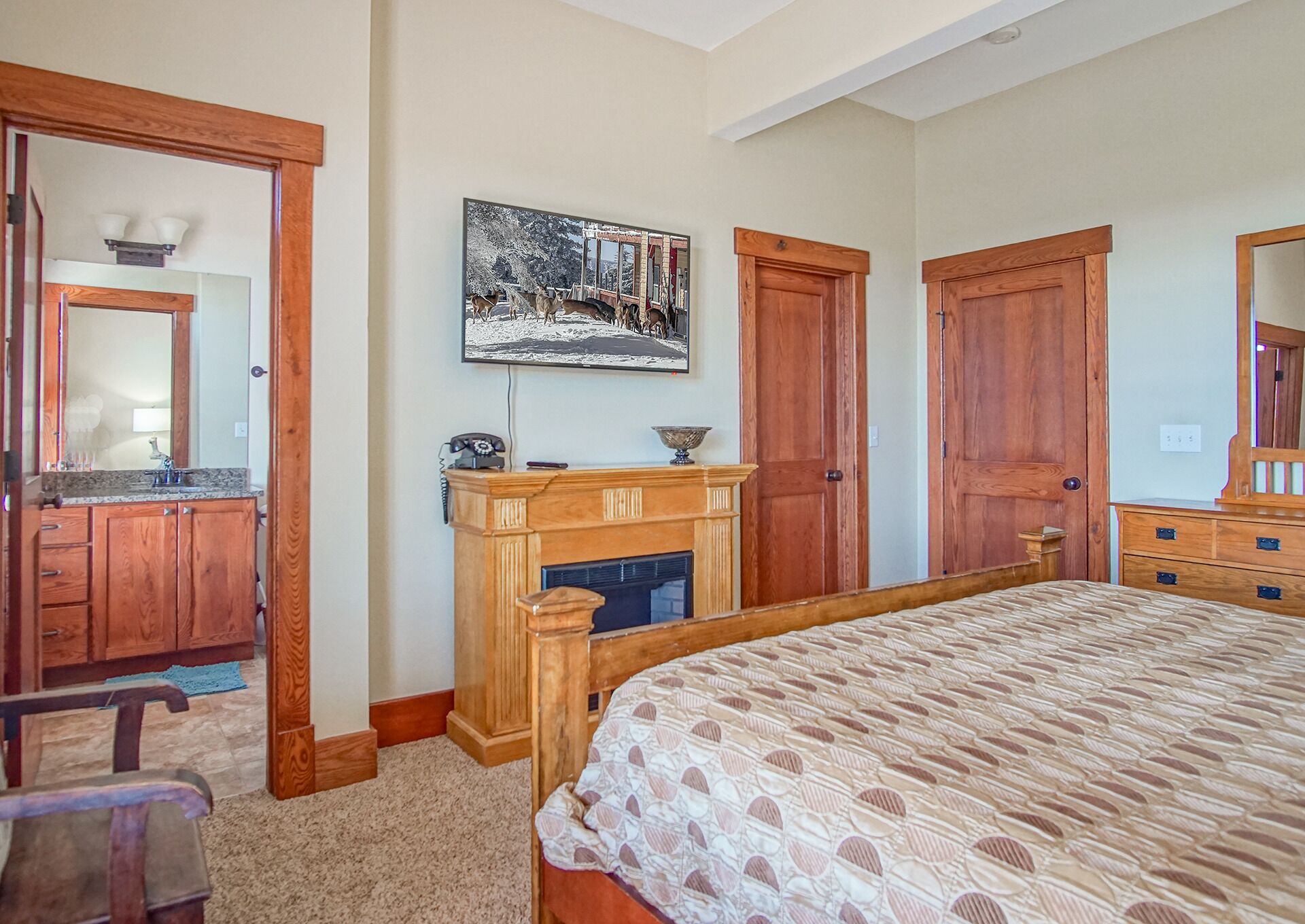 A bedroom with a large bed, wooden wardrobe, a fireplace, and a painting of a snowy landscape.