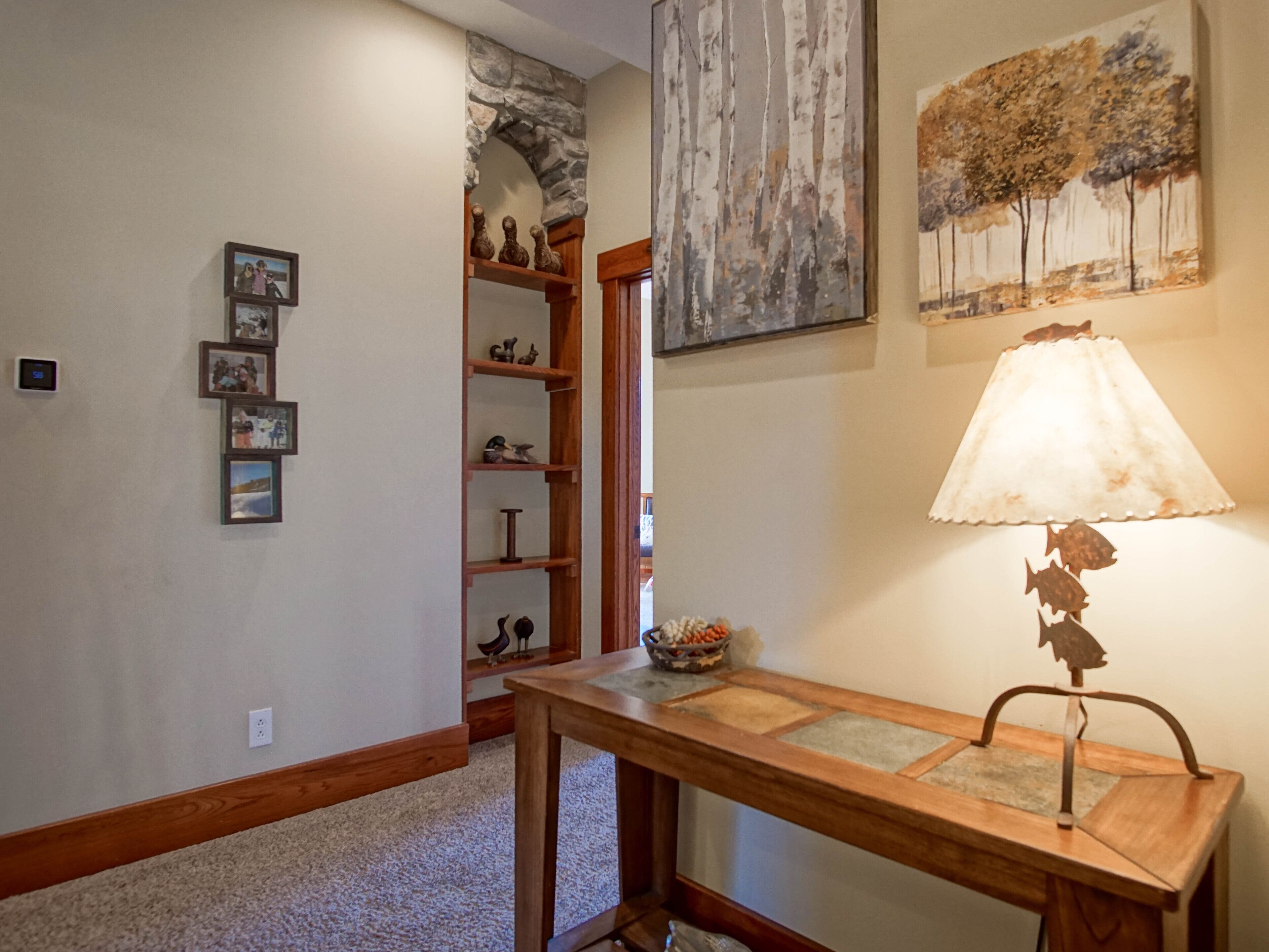 A hallway with a wooden table, a stone archway, and a wall with framed pictures.