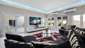 Un salon moderne avec un téléviseur à écran plat, une table basse en verre et un canapé agrémenté de coussins en fausse fourrure.