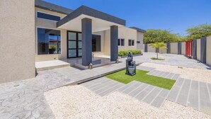 Un bâtiment moderne doté d’un patio couvert, d’un petit jardin avec un arbre et d’un chemin de gravier.