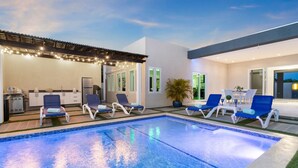 Un espace piscine extérieur moderne, doté de chaises longues, d’une cuisine et d’une terrasse avec une table et des chaises.
