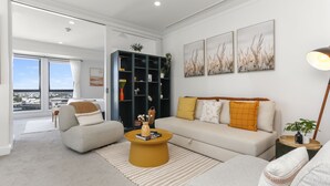 A modern living room with a sofa, armchair, and coffee table, a bookshelf, and artwork on the wall. - Urban Retreat in the Heritage Building (Auckland)
