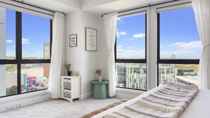 A modern bedroom with large windows, a bed with a striped blanket, a small side table with a vase, and a white dresser. - Urban Retreat in the Heritage Building (Auckland)