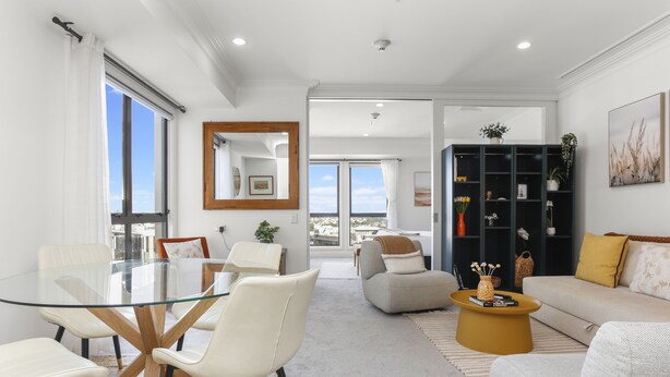 A modern living room with a glass dining table, white sofas, and a black bookshelf. - Urban Retreat in the Heritage Building (Auckland)