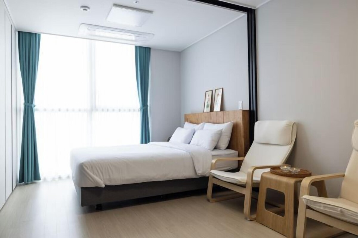 Une chambre d’hôtel moderne avec un lit, deux chaises, une petite table et une fenêtre avec des rideaux.