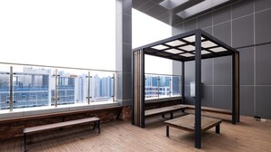 A modern interior with a wooden floor, a wooden bench, a metal pergola, and a view of a cityscape through large windows. - Grandbleu Hotel & Residence (Incheon)