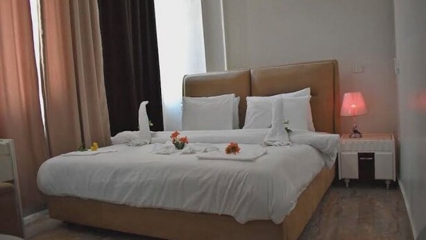A neatly made bed with white linens, a bedside table with a lamp, and a small vase with flowers. - City center hotel Cairo  (Cairo)