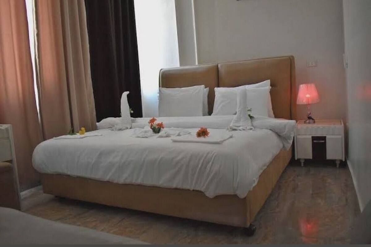 A neatly made bed with white linens, a bedside table with a lamp, and a small vase with flowers.