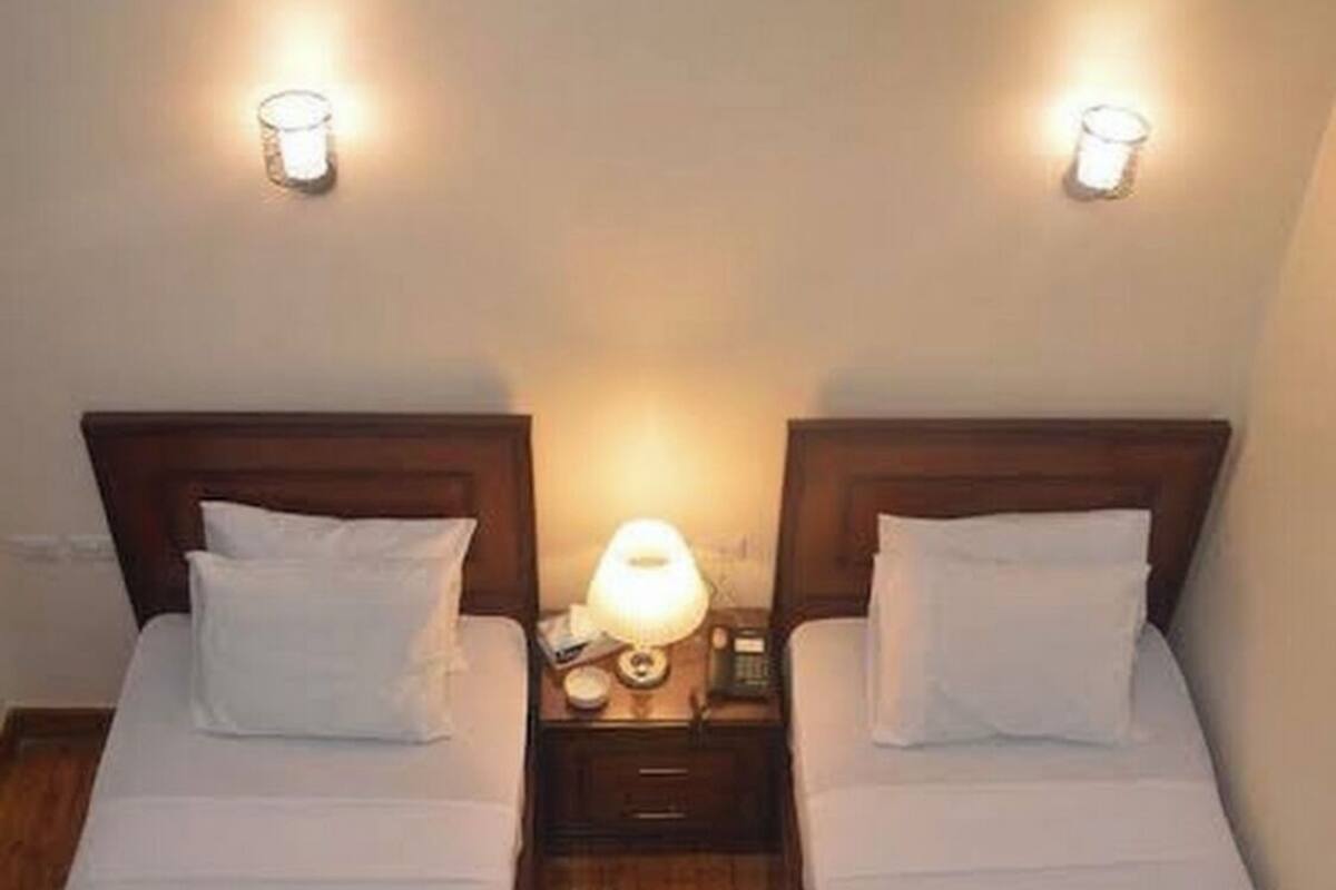 Two twin beds with white linens and towels, wooden headboards, and bedside lamps.