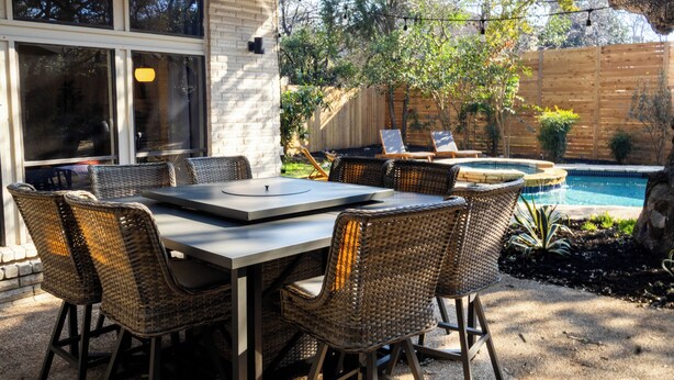 Um pátio externo com mesa de jantar e cadeiras de vime, piscina e cerca de madeira.