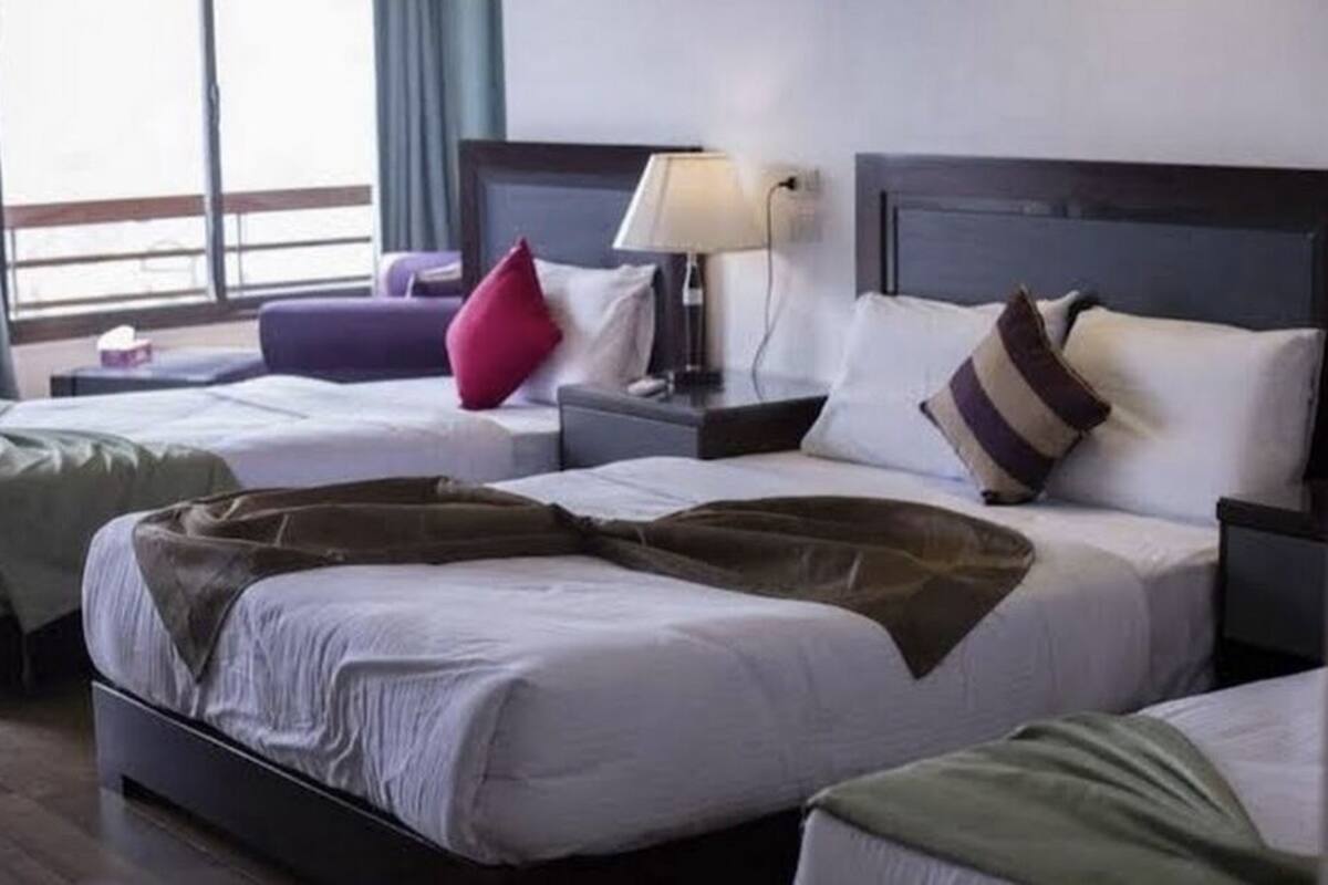 A hotel room with two beds, a nightstand with a lamp, and a view of the outside through large windows.