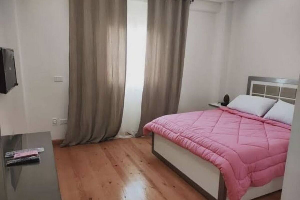 A bedroom with a bed, a bedside table, and a window with curtains.