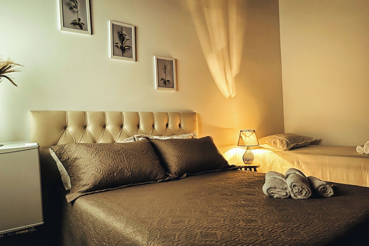 Un cuarto de hotel con una cama grande, una mesita de noche, una lámpara y dos cuadros en la pared.