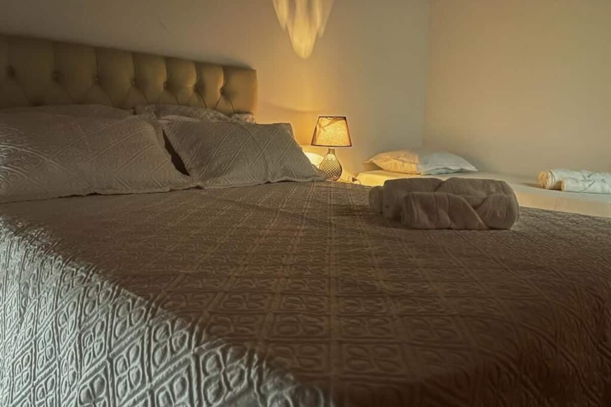 Una cama bien hecha con una colcha estampada, un cabecero capitonado y una lámpara de noche.