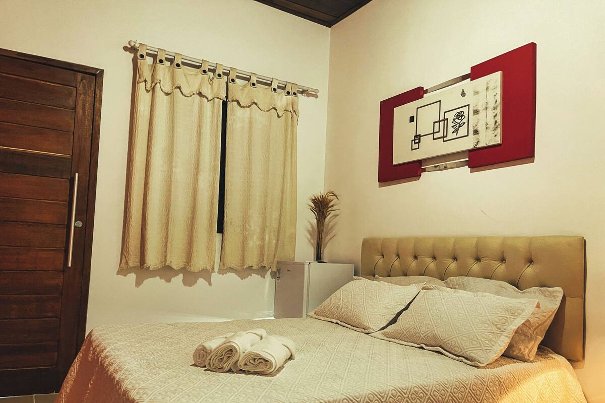 Un dormitorio con cama, cortinas, un cuadro en la pared y una puerta.