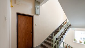 A staircase with a glass railing, a wooden door, and a utility box on the wall.