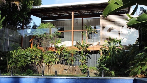 A pool with clear water, surrounded by tropical plants and a modern building with large windows.