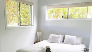 A bedroom with a bed, two windows, a ceiling fan, and a nightstand with a lamp.