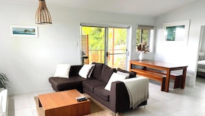 A modern living room with a dark brown sofa, a wooden coffee table, and a dining table with chairs.