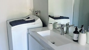 A modern bathroom with a white sink, a mirror, and a washing machine.