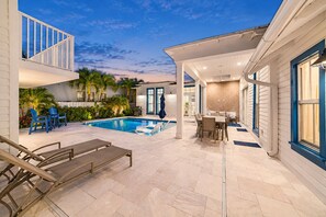 A pool area with lounge chairs, a dining table, and a covered patio.