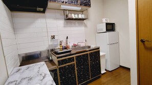 Een koelkast, een magnetron, een waterkoker, kookgerei, borden en bestek