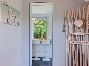 A doorway leading to a room with two white bar stools, a window with a view of greenery, and a wall with a 'BIENVENUE' sign.