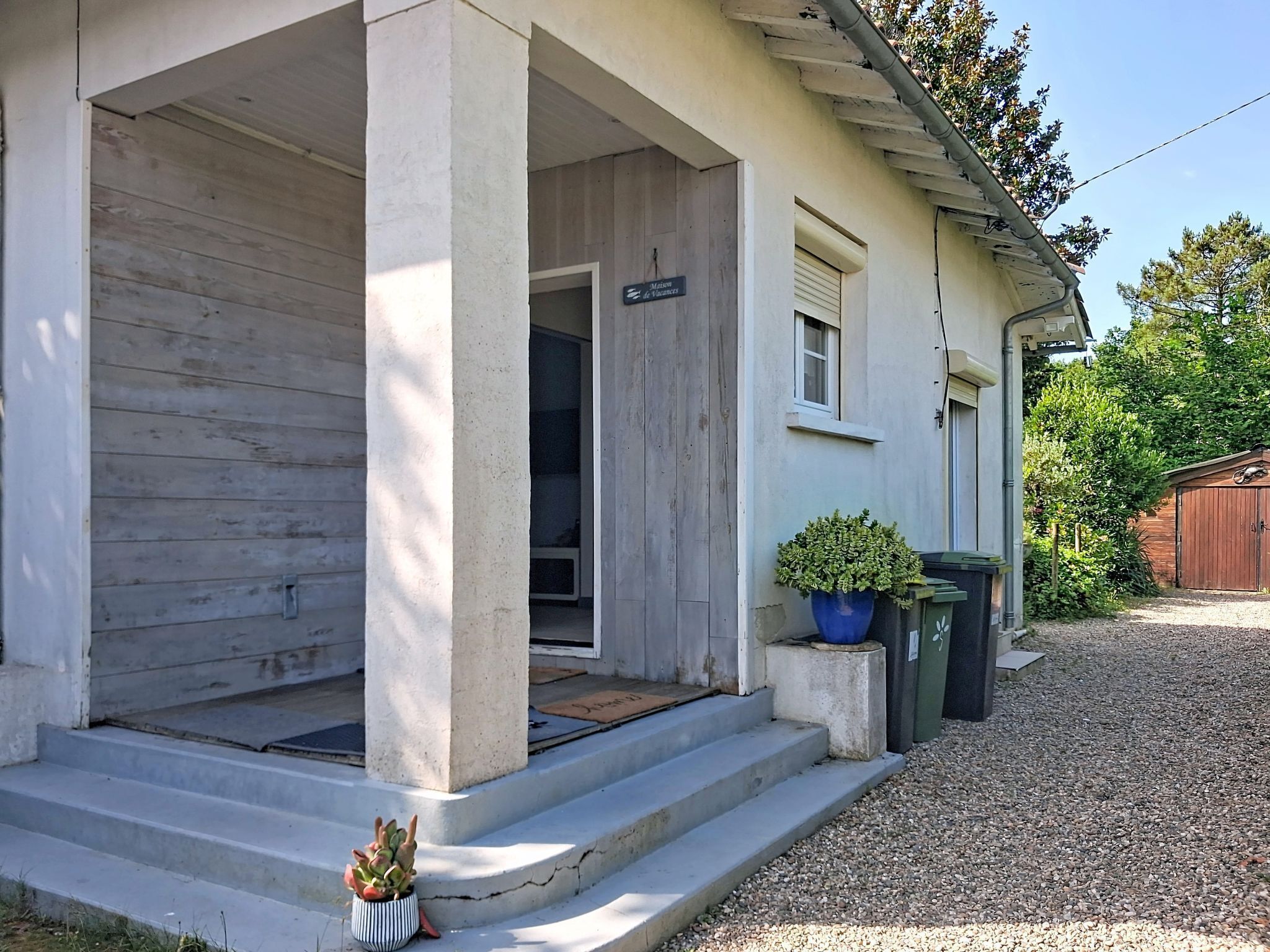 A building with a porch, a door, and a small garden area with plants.
