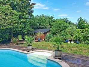 Une piscine entourée de plantes en pot et bordée d’une terrasse en bois.